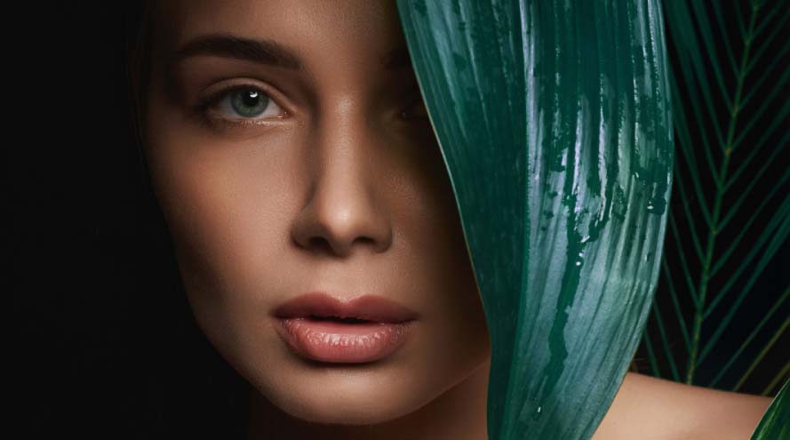 A woman with green leaves artistically arranged on her face, creating a natural and serene appearance.