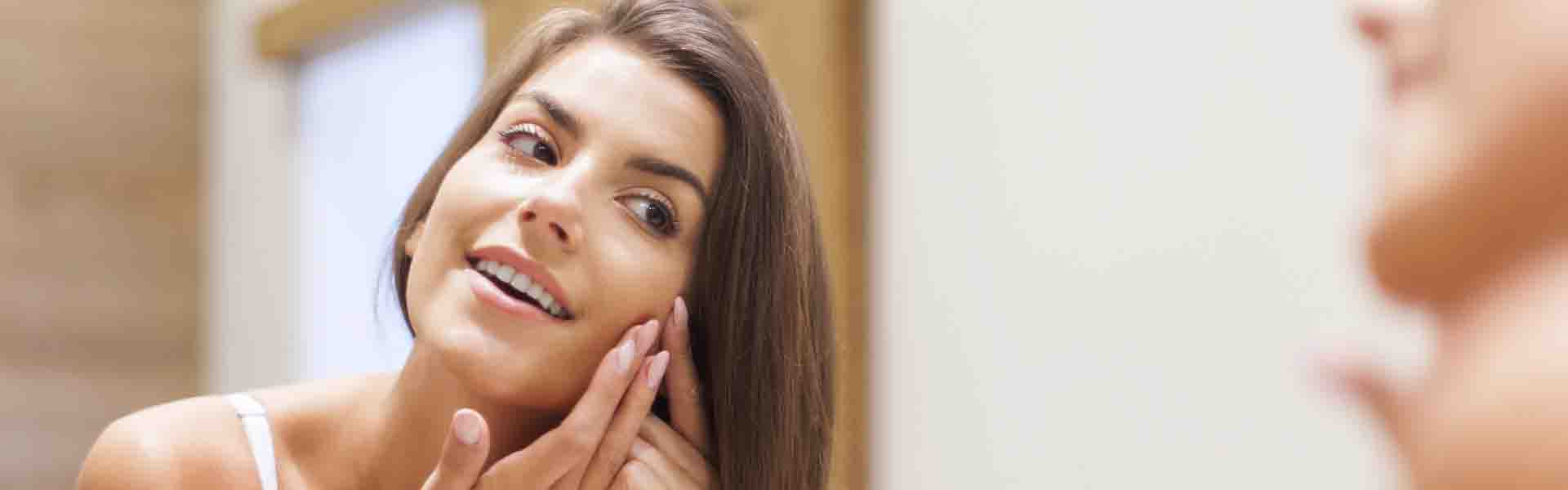 A woman gazes at her reflection in the mirror, examining her features with a thoughtful expression.