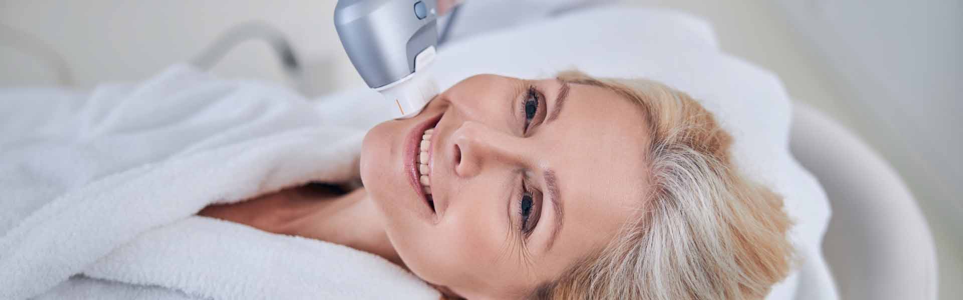 A woman enjoys a facial treatment, smiling as she relaxes in a serene spa environment.