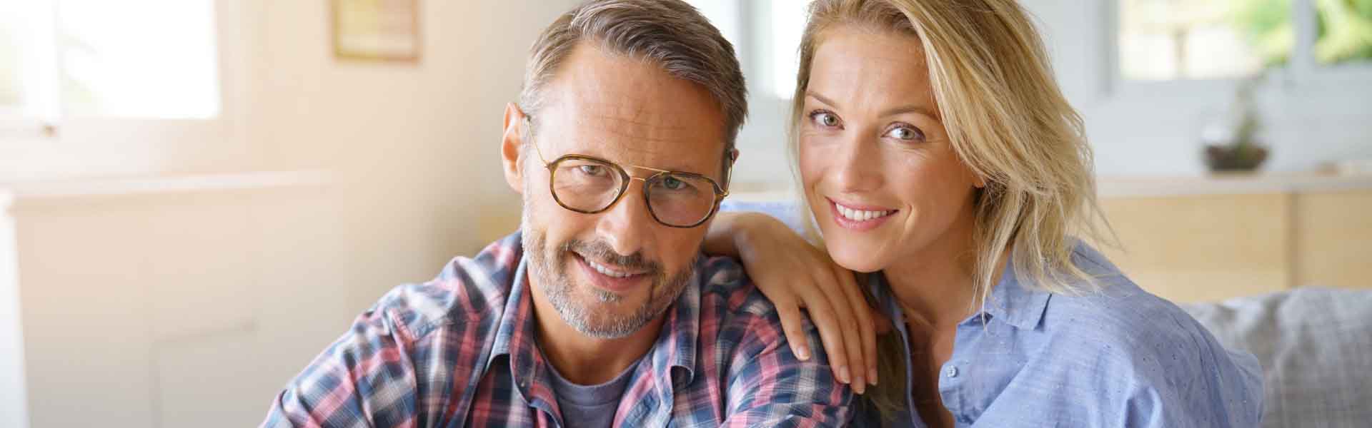 A cheerful man and woman pose for the camera, both displaying bright smiles that convey warmth and joy.