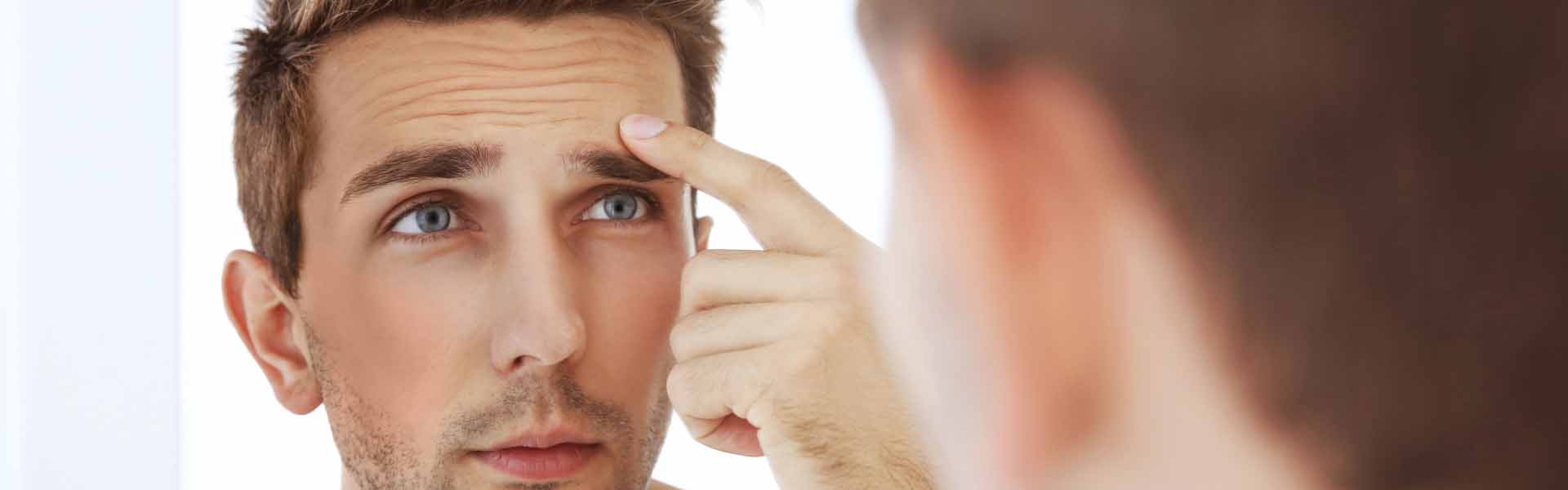 A man gazes at his reflection in the mirror, examining his facial features with a thoughtful expression.