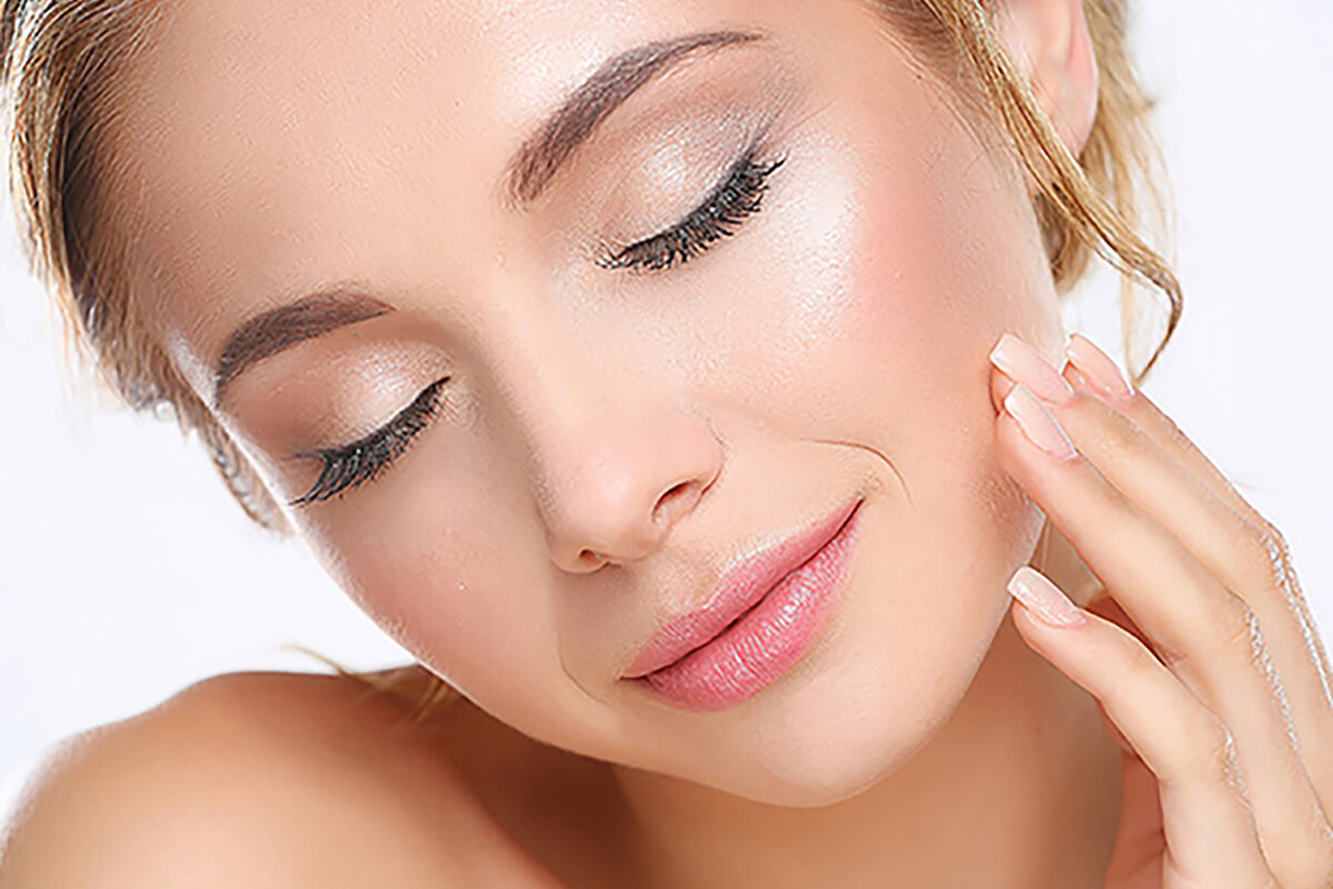 Woman with smooth, youthful skin gently touching her face after dermal filler wrinkle treatment in Gardner, MA